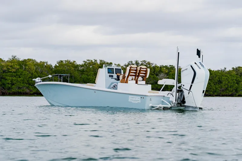  Yacht Photos Pics 2026 Broadwater 25 Bay Cat boat on calm water near lush greenery.