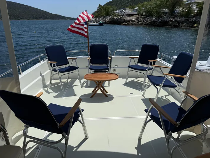 Wahoowa Yacht Photos Pics 2019 Back Cove Downeast boat deck with chairs, table, and American flag, overlooking scenic water.