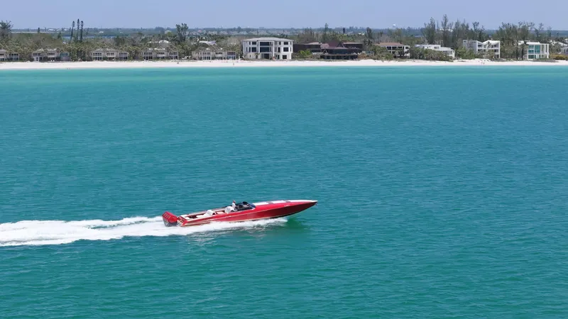 Lady Lisa Yacht Photos Pics Red 2023 Nor-Tech 55 Flyer speedboat cruising on turquoise water near a sandy beach.