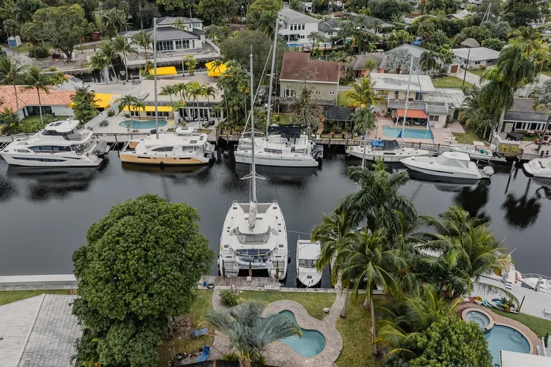  Yacht Photos Pics Aerial view of Lagoon 46 catamaran docked in a scenic marina, surrounded by lush greenery.