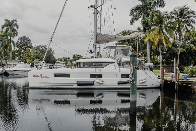  Yacht Photos Pics 2022 Lagoon 46 catamaran "Jungle Goddess" docked by palm trees, reflecting on calm water.