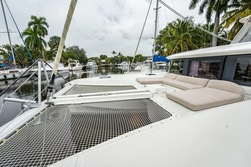  Yacht Photos Pics 2022 Lagoon 46 catamaran with spacious deck and netting, docked near palm trees.