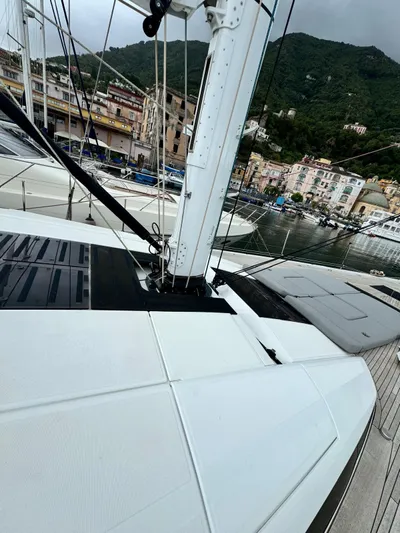 Blue Art Yacht Photos Pics 2023 Jeanneau 65 yacht docked in a scenic harbor with lush hills.