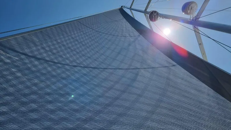 Blue Art Yacht Photos Pics Sail of 2023 Jeanneau 65 yacht against a bright blue sky and sun.