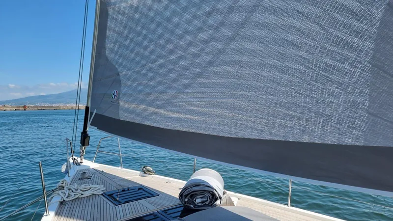Blue Art Yacht Photos Pics 2023 Jeanneau 65 sailboat on calm waters with raised sail and clear sky.