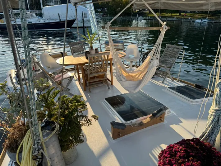 Pacific High Yacht Photos Pics Deck of 1983 Custom 62 sailboat with hammock, table, chairs, and plants by the water.