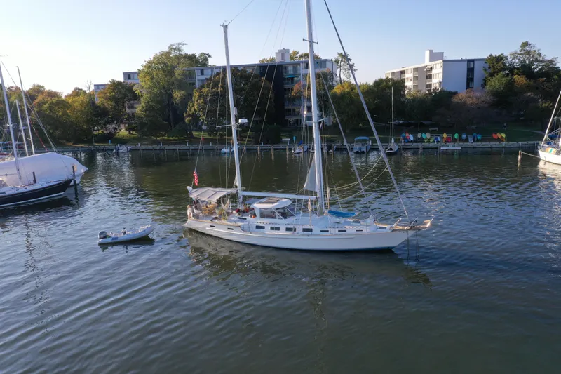 Pacific High Yacht Photos Pics Sailboat on calm water near shoreline, Custom 62 model, 1983, with buildings in the background.