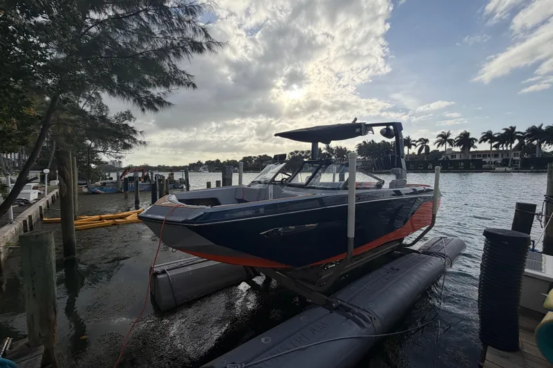 Coastal Edition Yacht Photos Pics 2022 Nautique Super Air Nautique G25 boat docked by waterfront under cloudy sky.