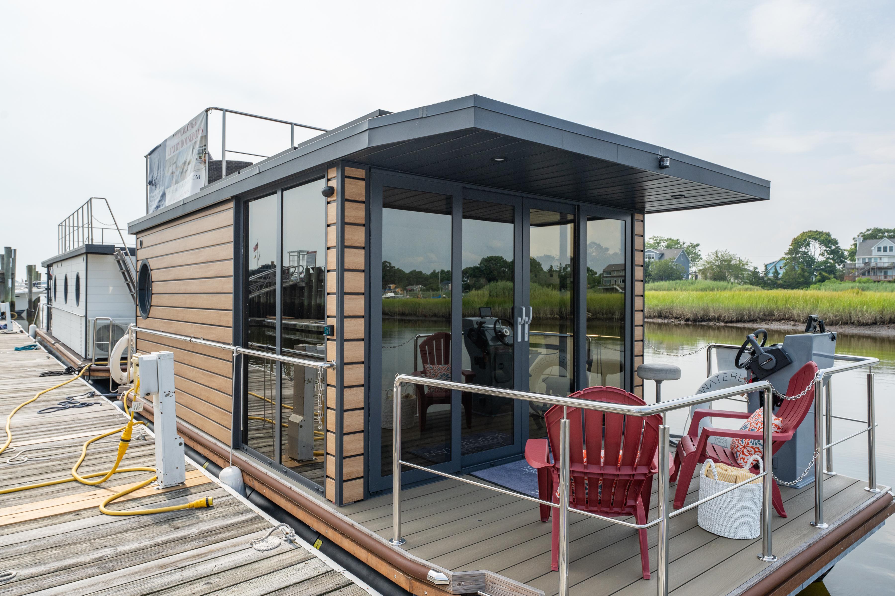 Modern 2024 Waterlodge Apart M houseboat docked, featuring glass doors and outdoor seating.