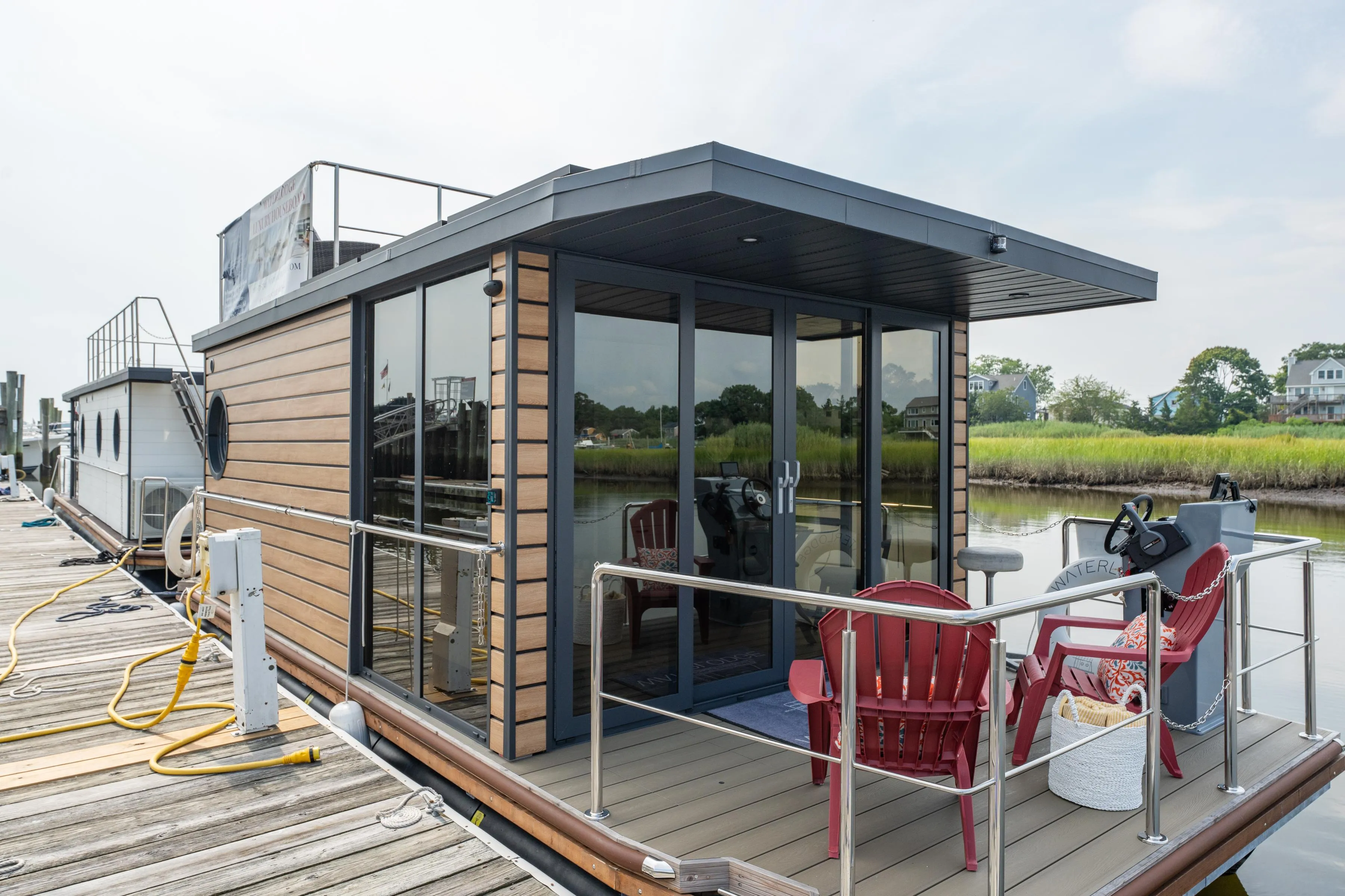 Modern 2024 Waterlodge Apart M houseboat docked, featuring glass doors and outdoor seating.