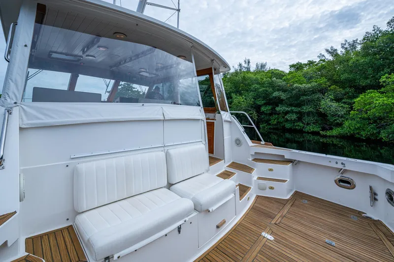 Bright Star Yacht Photos Pics 2003 Grand Banks 49 Eastbay HX yacht with white seating and wooden deck, near lush greenery.