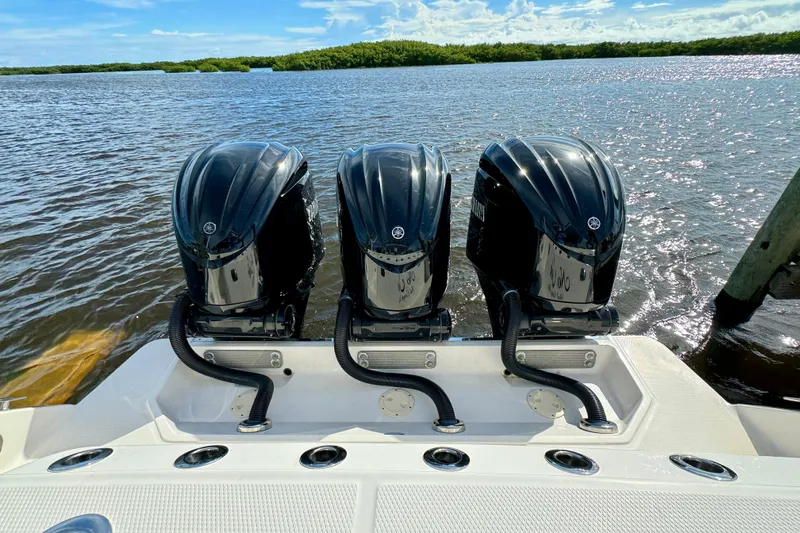 No Joke Yacht Photos Pics Triple outboard engines on a 2022 Robalo R360 Center Console boat, docked by the water.