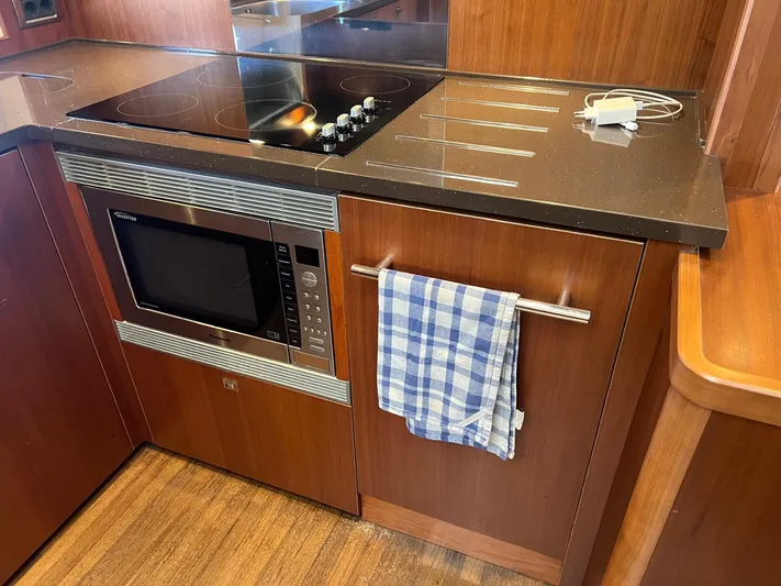  Yacht Photos Pics Modern yacht kitchen with induction cooktop, microwave, and checkered towel on wooden cabinetry.