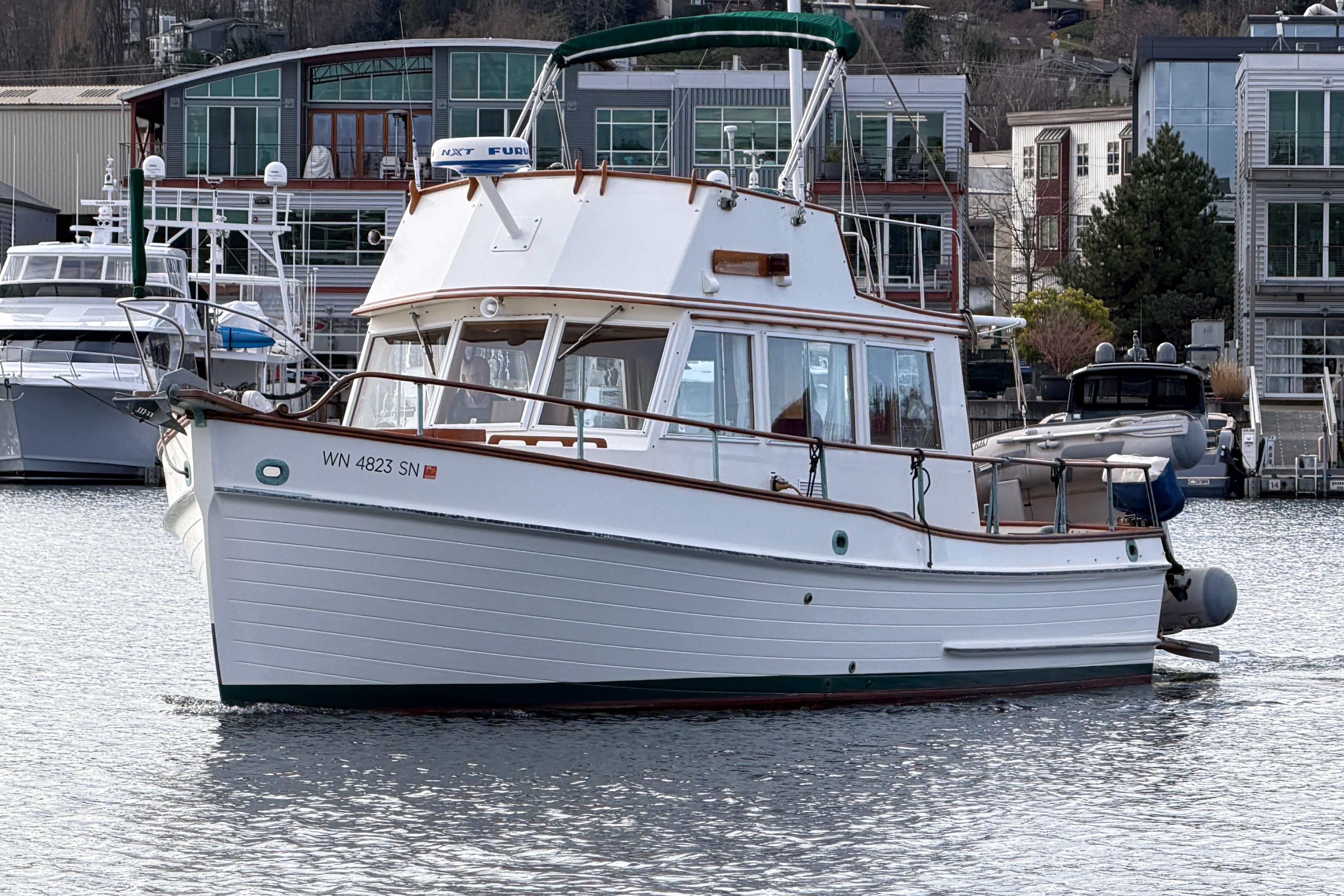 1981 Grand Banks 32 Sedan boat docked in a marina, surrounded by modern buildings.