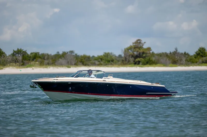  Yacht Photos Pics 2022 Chris-Craft Launch 27 boat cruising on calm water near a sandy shoreline.