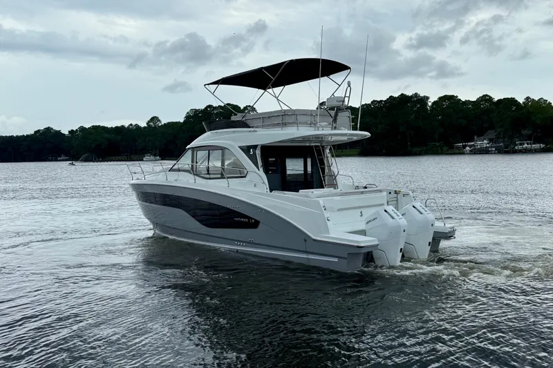  Yacht Photos Pics 2026 Beneteau Antares 12 yacht cruising on a serene lake with lush forest backdrop.