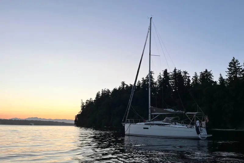 A Bientot Yacht Photos Pics 2016 Jeanneau Sun Odyssey 349 sailboat at sunset near forested shoreline.