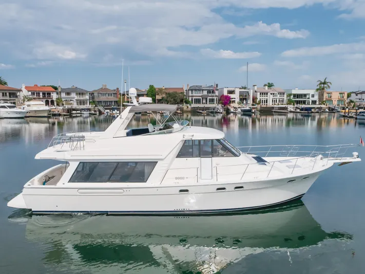 Coffey To Cocktails II Yacht Photos Pics 1998 Bayliner 4788 Pilot House Motoryacht on calm water, with waterfront homes in the background.