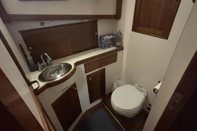 Oasis Yacht Photos Pics 1987 Wilbur 38 yacht bathroom with wooden cabinetry, stainless steel sink, and compact toilet.