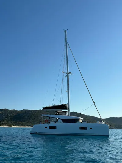  Yacht Photos Pics 2024 Lagoon 42 catamaran sailing on clear blue waters with scenic mountain backdrop.