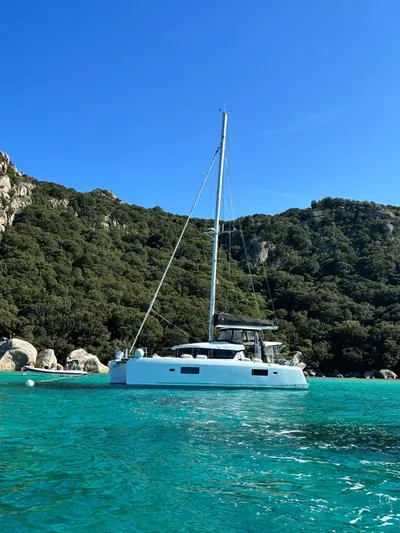  Yacht Photos Pics 2024 Lagoon 42 catamaran anchored in turquoise waters, surrounded by lush green hills.