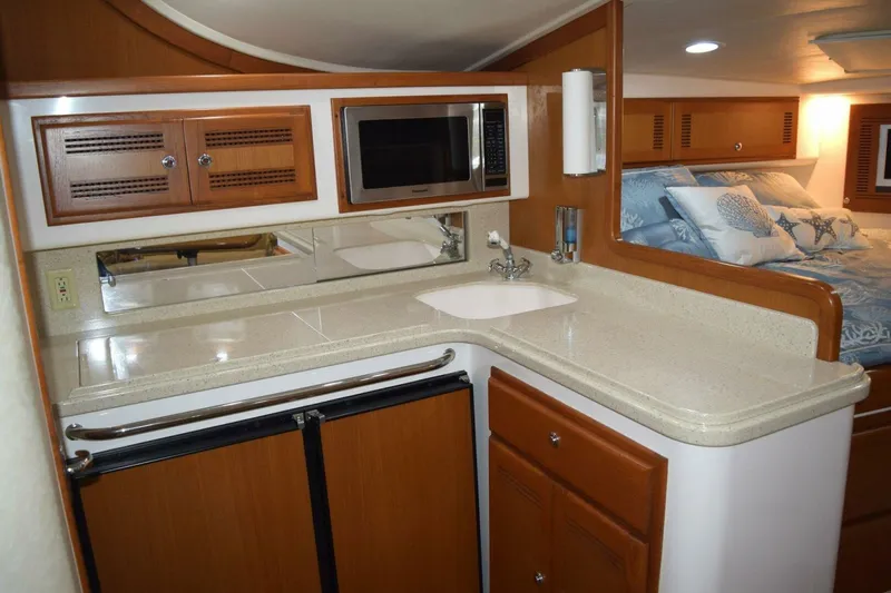 Never Again VII Yacht Photos Pics 2006 Cabo 35 Express yacht interior with kitchenette, featuring wood cabinets, microwave, and cozy sleeping area.