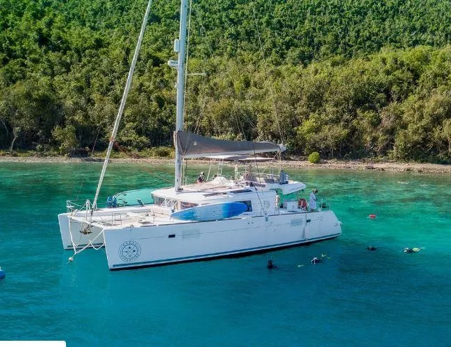 Great Adventure Yacht Photos Pics 2014 Lagoon 450 catamaran anchored in clear turquoise water near a lush green shoreline.