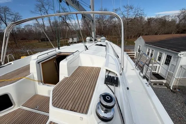 Recovery Room Yacht Photos Pics 2019 Jeanneau 51 sailboat deck with teak flooring and open hatch, docked near a house.