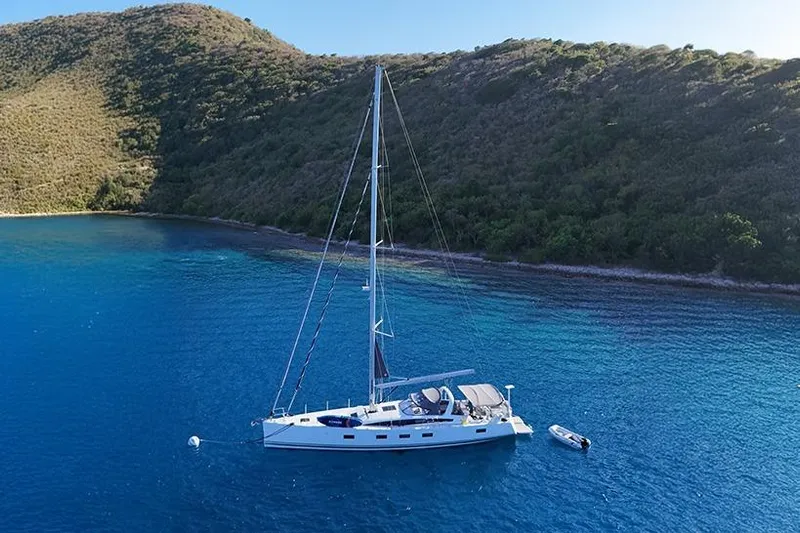 Miss Fiona Yacht Photos Pics 2020 Jeanneau 64 yacht anchored in clear blue waters near a lush hillside.