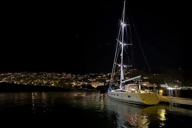 Miss Fiona Yacht Photos Pics 2020 Jeanneau 64 yacht docked at night, illuminated against a cityscape backdrop.
