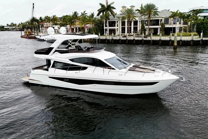 Bugsy Yacht Photos Pics 2020 Galeon 550 Fly yacht cruising on a scenic waterfront with palm trees.