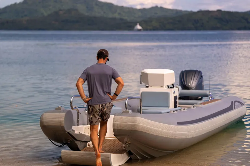 Dream Yacht Photos Pics Man boarding Abeking & Rasmussen 6430 boat, 2001 model, on a serene lake with distant hills.