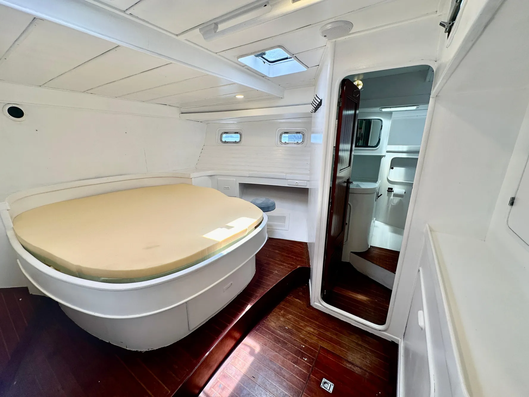 1983 Tayana 55 yacht interior with bed, wooden flooring, and white walls.