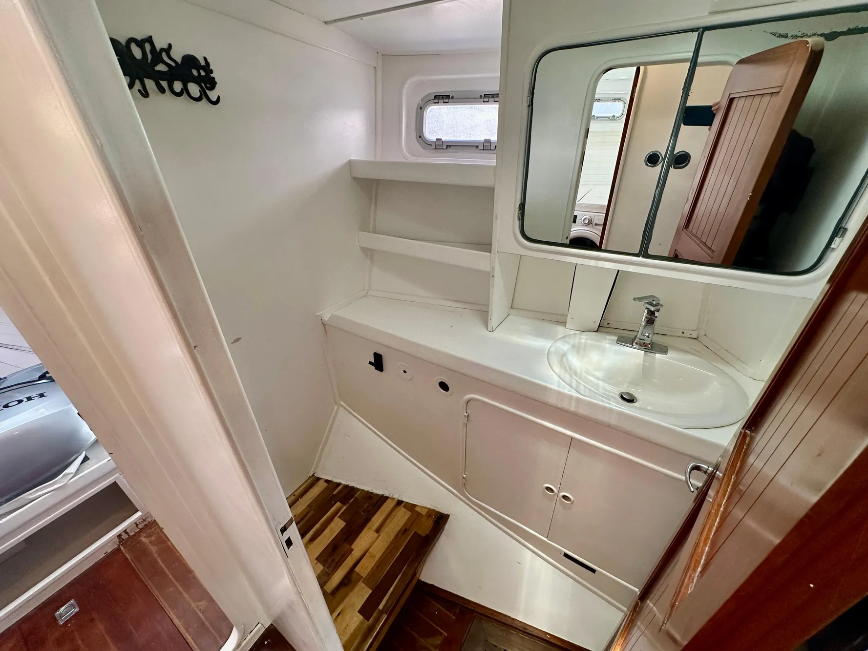 Bathroom interior of 1983 Tayana 55 yacht with sink, mirror, and wooden flooring.