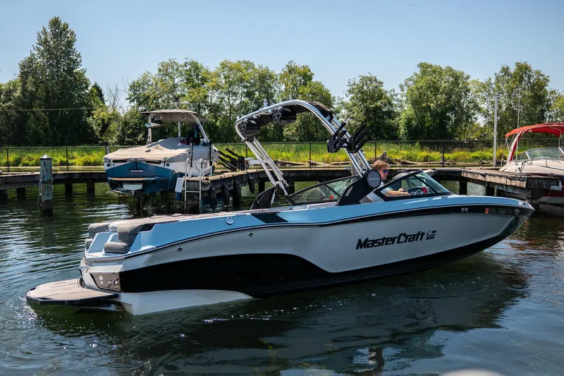  Yacht Photos Pics 2022 MasterCraft XT24 boat on water near dock, surrounded by trees.