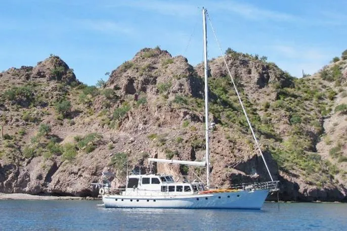 Custom 1991 Centre Cockpit Pilot House Steel Cutter Motorsailer near rocky coastline.