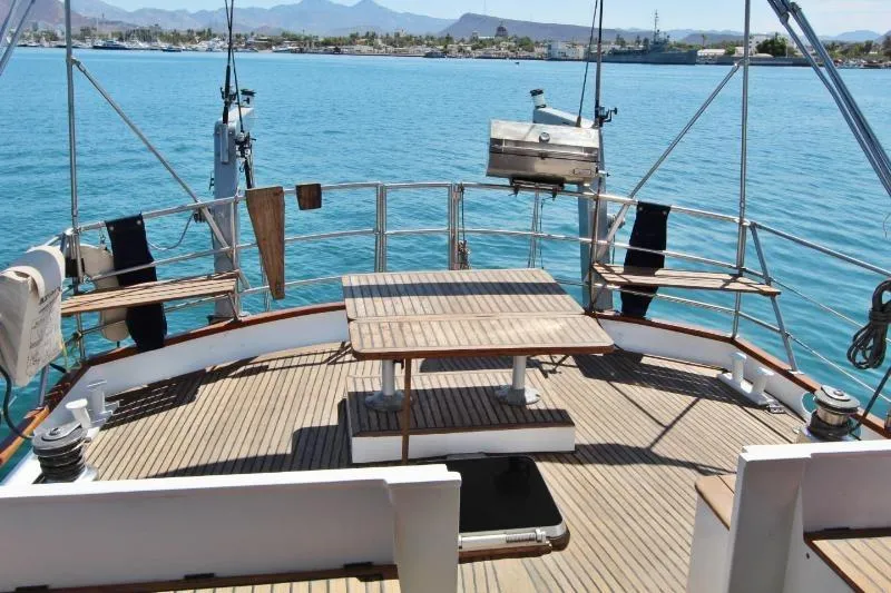 Ocean Villa Yacht Photos Pics Centre cockpit of 1991 Custom Motorsailer with wooden deck and table, overlooking calm blue waters.