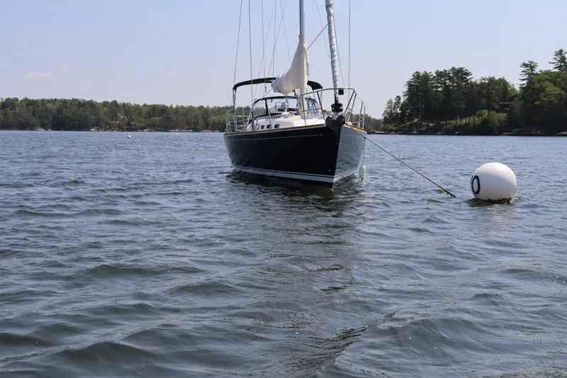 Cianna Yacht Photos Pics Sailboat Sabre 402 (2001) anchored on calm water near a buoy, surrounded by trees.
