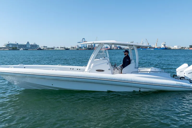  Yacht Photos Pics 2025 Airship 340 boat on water, with a person at the helm, port in background.