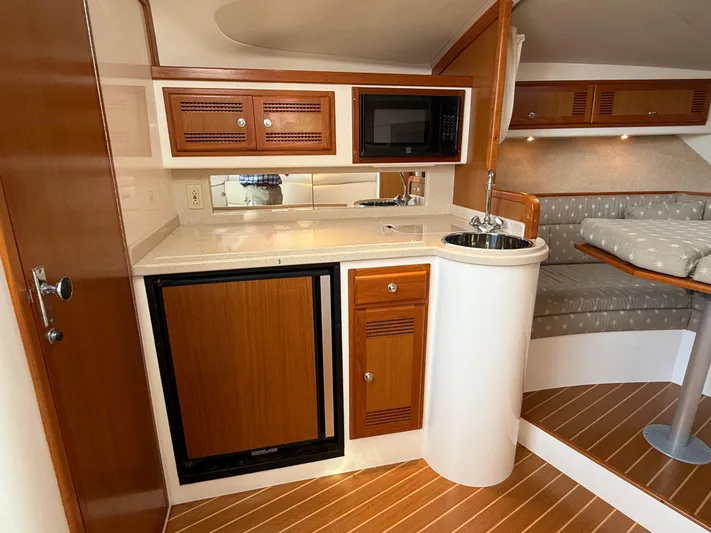 Club Car Yacht Photos Pics 1999 Cabo 31 Express yacht interior with kitchenette, featuring wood cabinets and seating area.