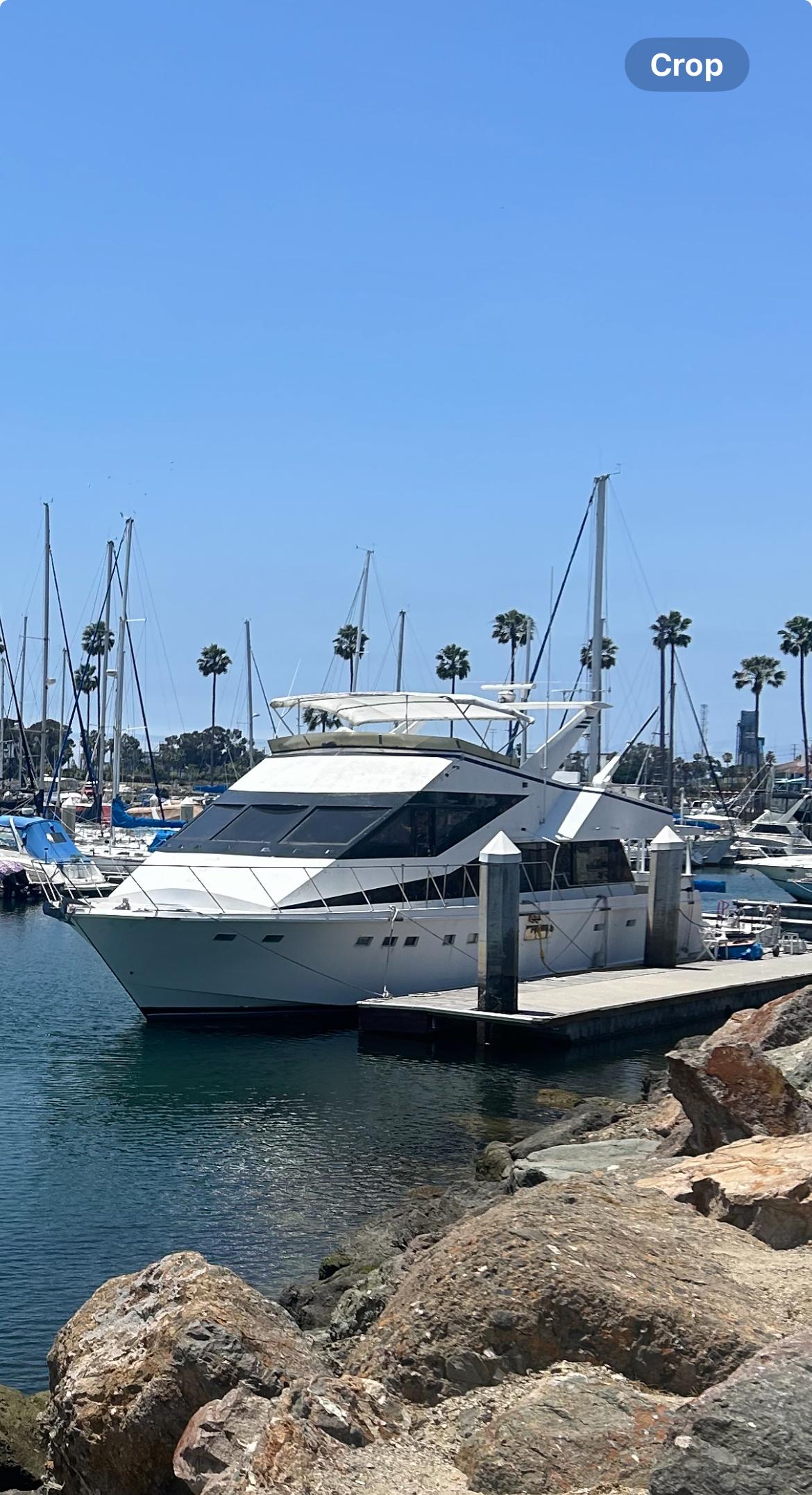 Luxury yacht docked in marina, clear blue sky, palm trees in background, 1989 custom model.