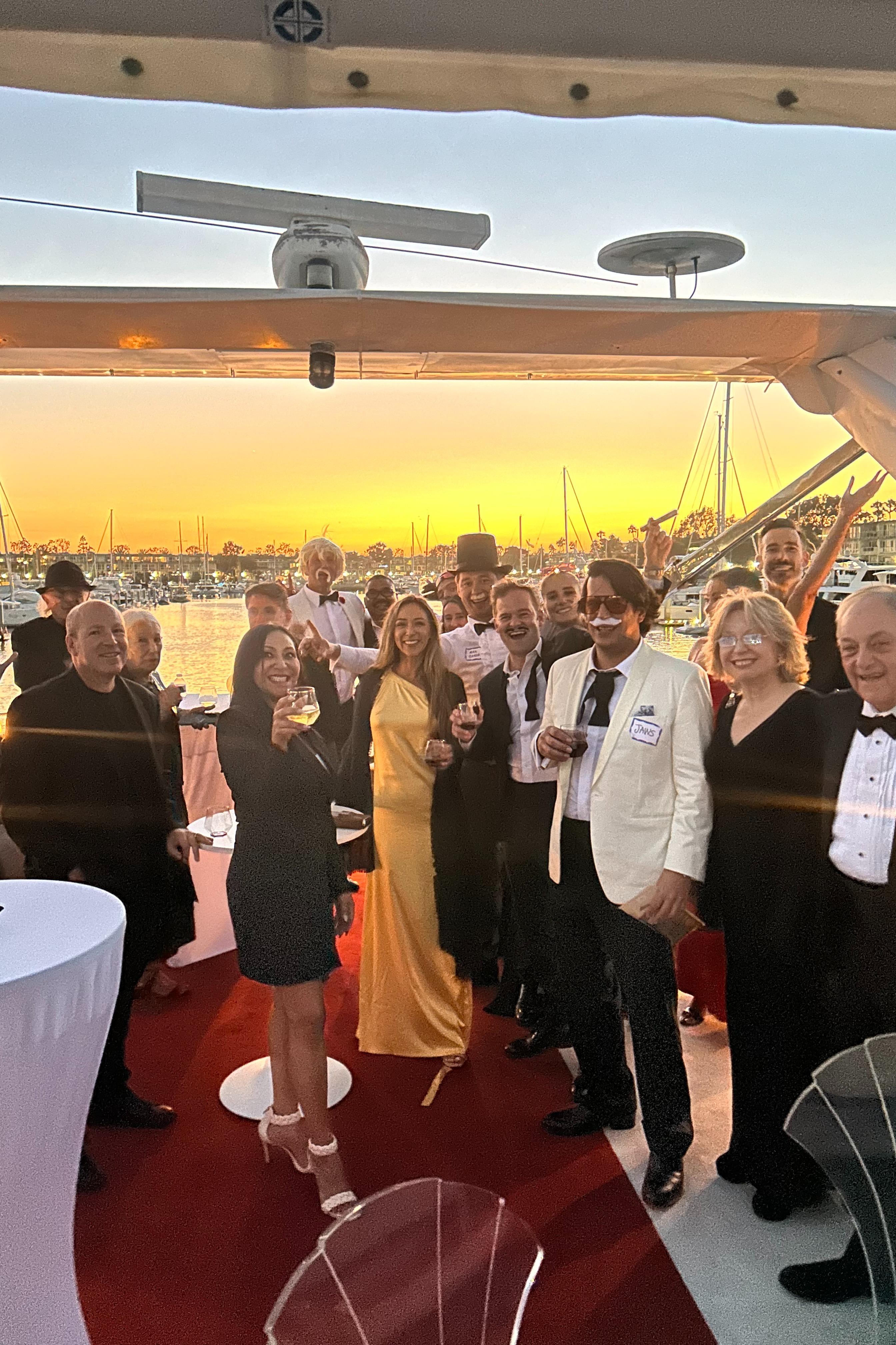 Group celebrating on a yacht at sunset, dressed in formal attire.