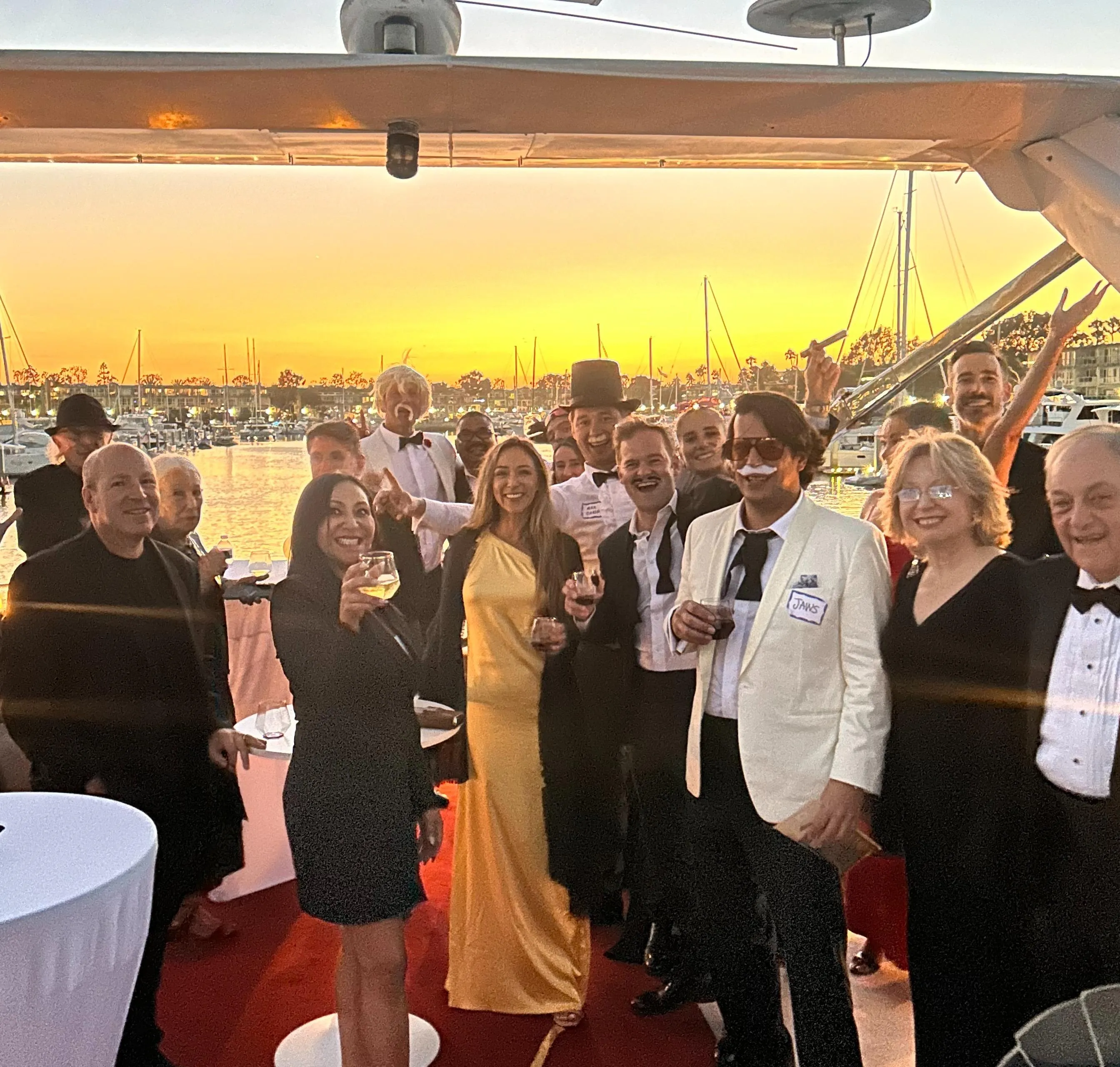 Group celebrating on a yacht at sunset, dressed in formal attire.