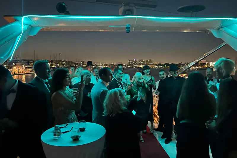 Scherzo Yacht Photos Pics Elegant yacht party at night with guests in formal attire, city skyline in background.