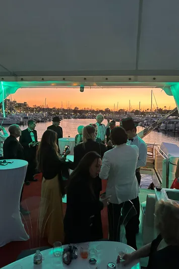 Scherzo Yacht Photos Pics People enjoying a sunset yacht party with elegant attire and vibrant lighting.