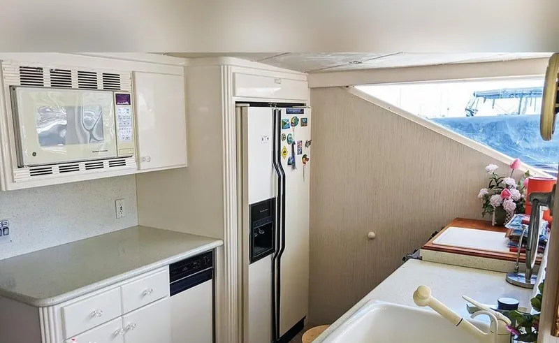 Scherzo Yacht Photos Pics Compact kitchen with white cabinets, microwave, refrigerator, and sink; bright window view.