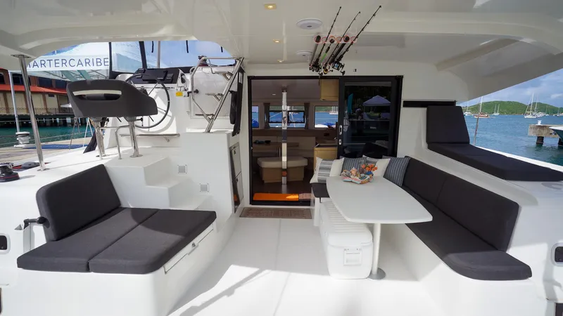 Good Times And Tan Lines Yacht Photos Pics 2023 Lagoon 42 yacht interior with seating, table, and helm station, docked by the water.