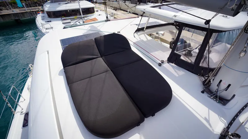 Good Times And Tan Lines Yacht Photos Pics 2023 Lagoon 42 yacht with black sunbed on deck, docked at marina.