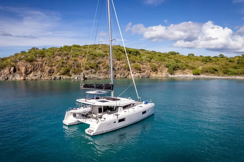 Good Times And Tan Lines Yacht Photos Pics 2023 Lagoon 42 catamaran anchored in serene turquoise waters near a lush island.