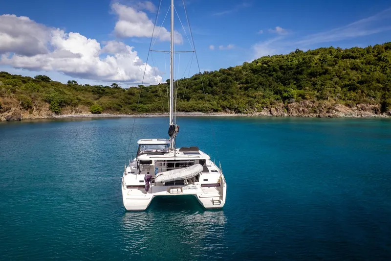 Good Times And Tan Lines Yacht Photos Pics 2023 Lagoon 42 catamaran anchored in serene turquoise bay with lush green hills.
